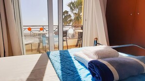 Et hotelværelse med seng, udsigt over det åbne område gennem en skydedør, samt en balkon med stole og borde.