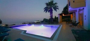 A swimming pool with a tiled deck, a palm tree, and a building with outdoor seating.