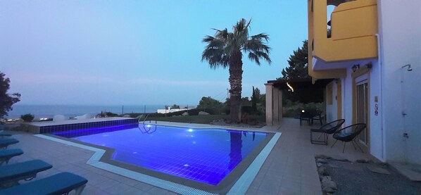Ein Pool mit Blick auf das Meer, umgeben von Palmen und einem Gebäude mit Außenplätzen.