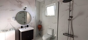 Ein Badezimmer mit rundem Spiegel, Waschbecken in Weiß, Toilette und Dusche.