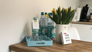 Eine Küchenzeile mit Holztischplatte, einem weißen Stuhl, einem flauschigen weißen Hocker, einer Serviertablett mit Gläsern, einer Topfpflanze und einem Schild mit Text.
