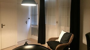 A room with a wicker chair, a hanging light fixture, a door, and a window with blinds. - Nice studio (La Rochelle)