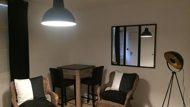 A dining area with a table and four chairs, a floor lamp, and a mirror on the wall. - Nice studio (La Rochelle)