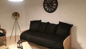 A room with a black sofa, a round wall clock, a hanging light, and a floor lamp. - Nice studio (La Rochelle)