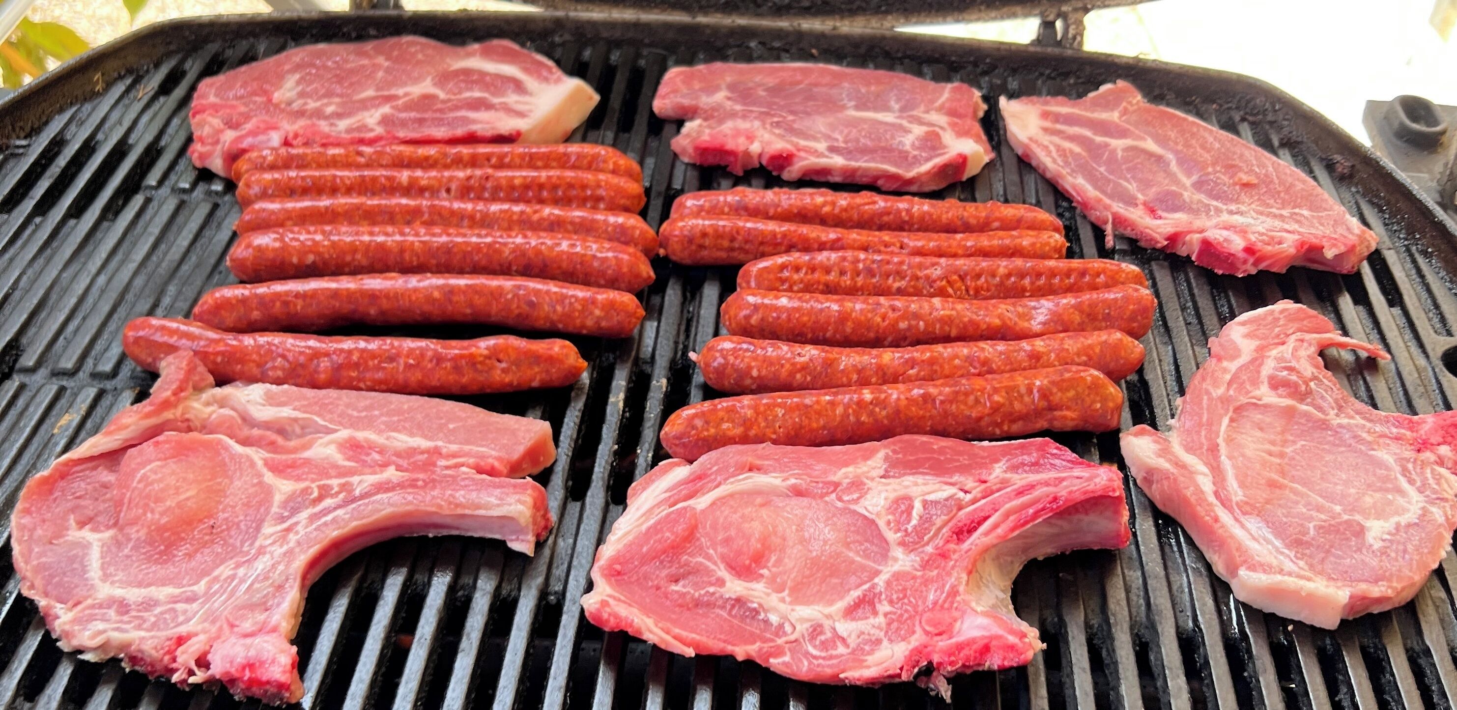 Carne cruda y salchichas en una parrilla.
