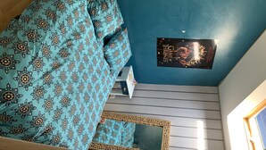 Un dormitorio con una pared azul, una cama con manta estampada, un cuadro enmarcado y un cartel en la pared.