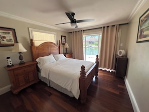 A bedroom with a wooden bed, a ceiling fan, a nightstand, a lamp, and a window with curtains.