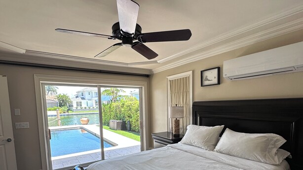 Ein Schlafzimmer mit einem großen Bett, einem Deckenventilator, einer Klimaanlage und Blick auf einen Swimmingpool.