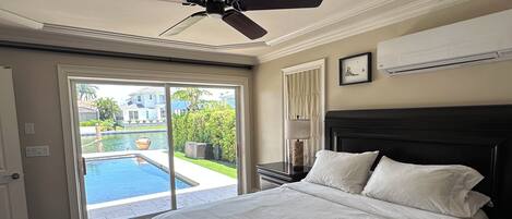 Un dormitorio con una cama grande, ventilador de techo, aire acondicionado y vista a una piscina.