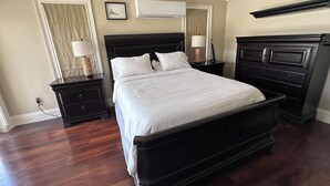 Ein Hotelzimmer mit einem großen Bett, zwei Nachttischen, einer Kommode, einer Klimaanlage und einem Deckenventilator.