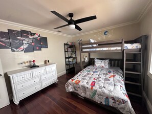 A bedroom with a bunk bed, a ceiling fan, a dresser, and a bookshelf.