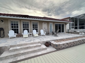 A covered outdoor patio with Adirondack chairs, a stone fire pit, and a stone staircase leading to a door.