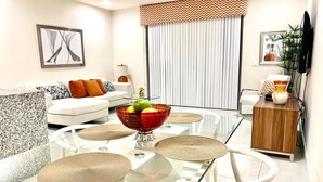 Ein modernes Wohnzimmer mit einem Glastisch, weißen Stühlen, einem weißen Sofa und einer Holzkommode.