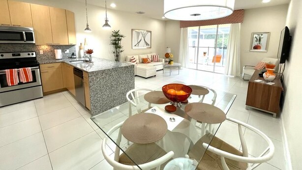 Eine moderne Küche mit Granit-Arbeitsplatten, Edelstahlgeräten und einem Essbereich mit Glastischen und weißen Stühlen.