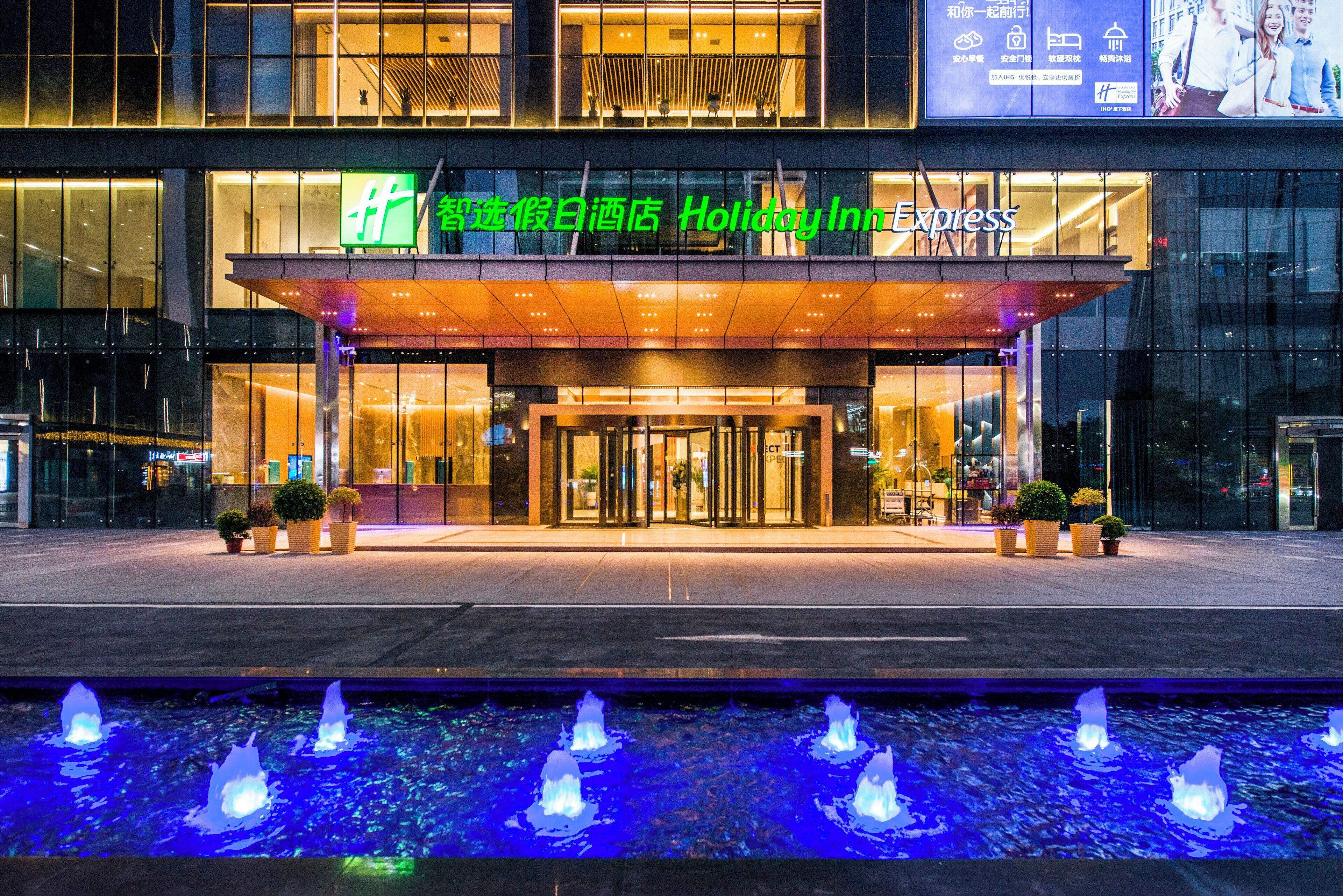 Ein Hotel mit Glasfassade, einem überdachten Eingangsbereich und einer Wasseranlage davor.