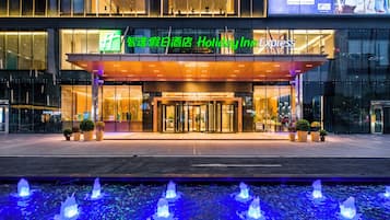 Ein Hotel mit Glasfassade, einem überdachten Eingangsbereich und einer Wasseranlage davor.