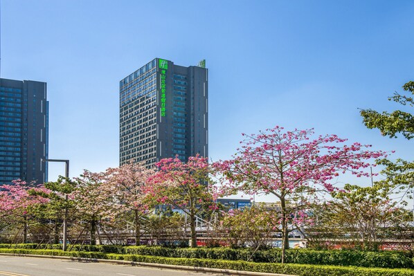 A modern building with a green sign, surrounded by blooming pink trees and a clear blue sky. - Holiday Inn Express Foshan Beijiao by IHG (Foshan)