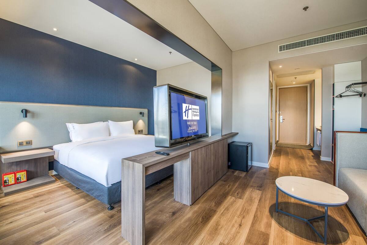 A modern hotel room with a large bed, bedside table, TV, and a small table.
