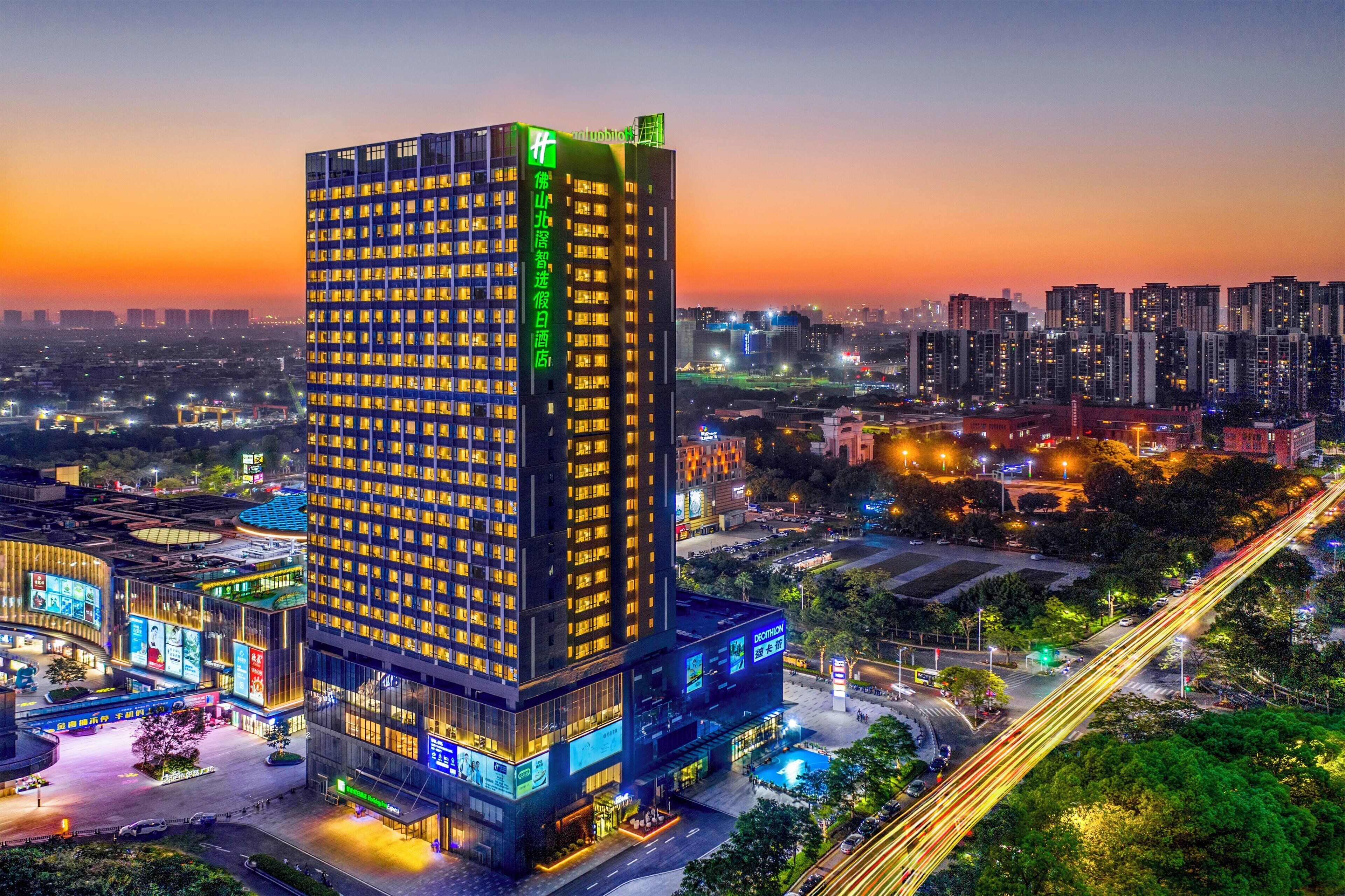 Un hotel moderno de gran altura con varios pisos, una entrada destacada y un paisaje urbano circundante al anochecer.
