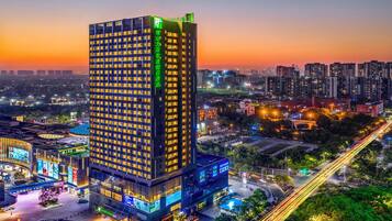 Un hotel moderno de gran altura con varios pisos, una entrada destacada y un paisaje urbano circundante al anochecer.