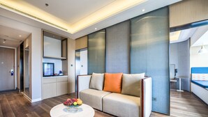Habitación de hotel moderna con sofá, una mesa redonda con fruta y vistas a la ciudad.