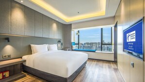 Una habitación de hotel moderna con una cama grande, vistas a la ciudad y un televisor en la pared.