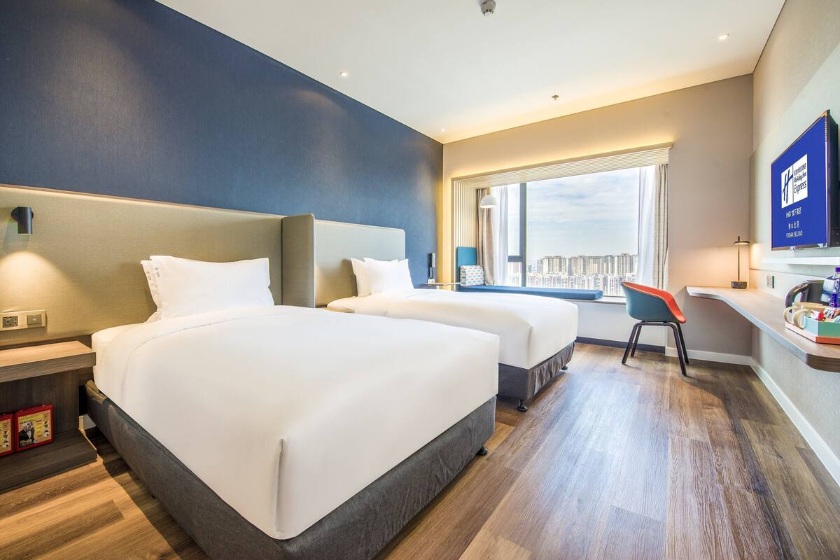 A hotel room with two beds, a desk, and a chair.
