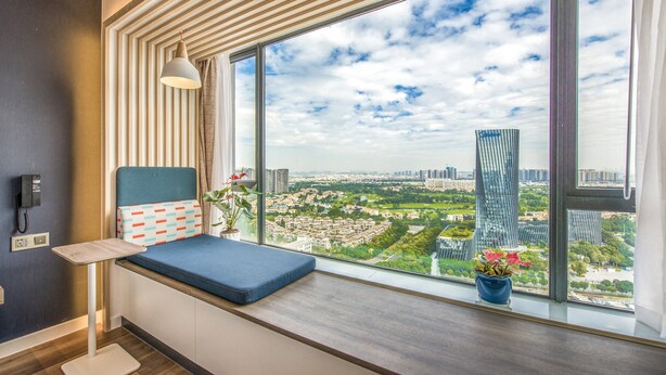 Una habitación moderna con un ventanal grande, un banco acolchado azul, una planta en maceta y un teléfono en la pared.