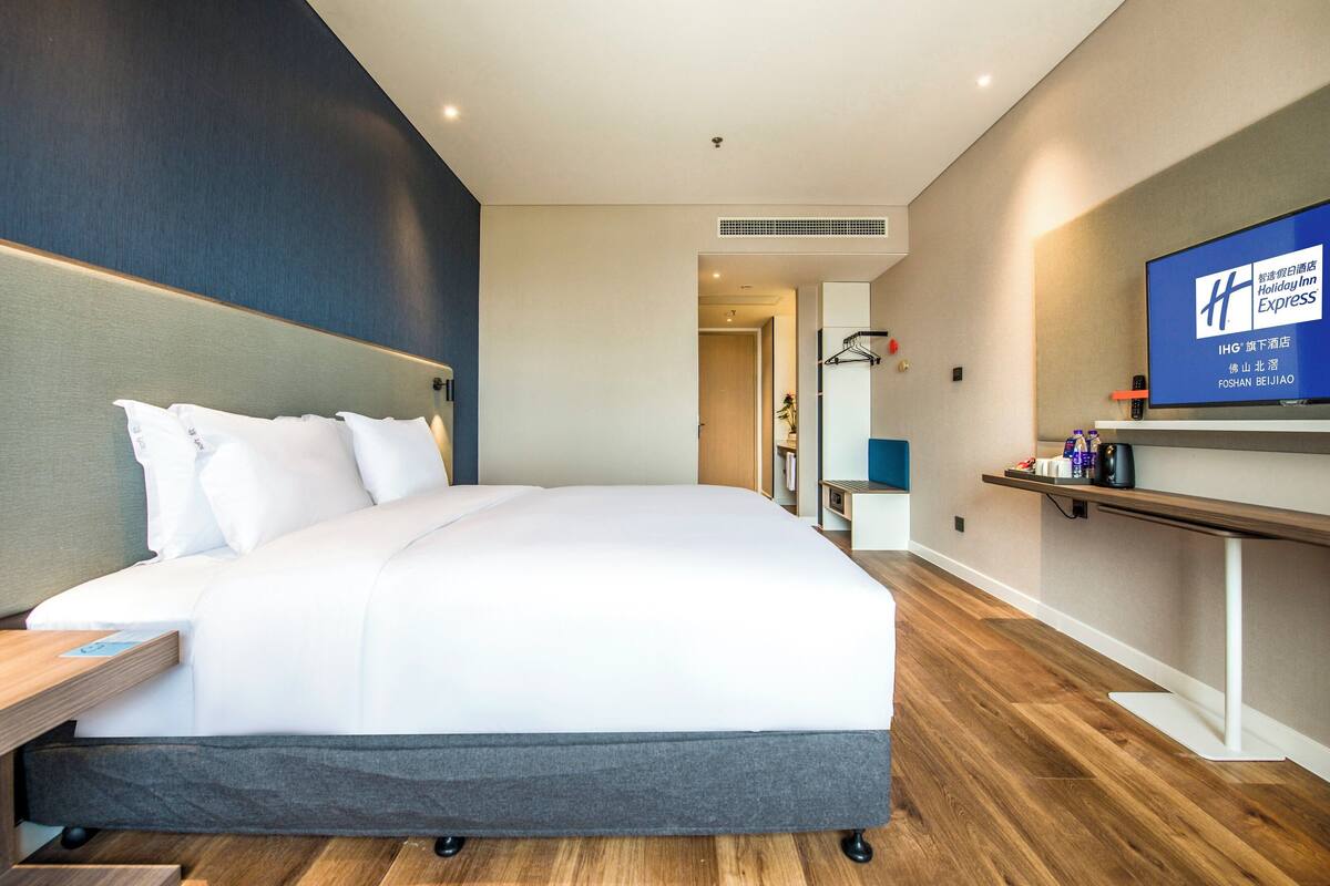A modern hotel room with a large bed, a television, and a wooden floor.
