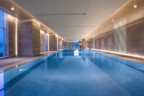 Ein langer, überdachter Schwimmbereich mit klarem, blauen Wasser, umgeben von Wänden mit einer strukturierten Oberfläche und einer Decke mit eingelassener Beleuchtung.