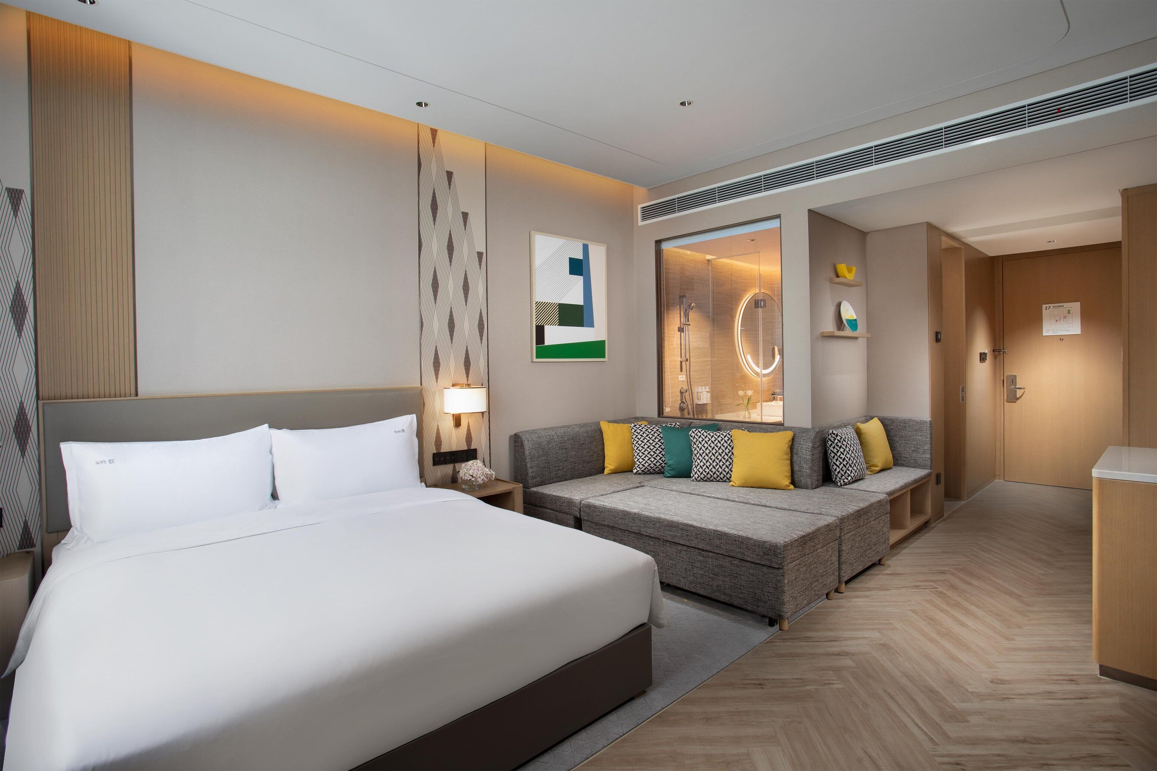 Ein Hotelzimmer mit einem großen Bett, einer Couch, einem Spiegel und einer kleinen Küchenzeile.