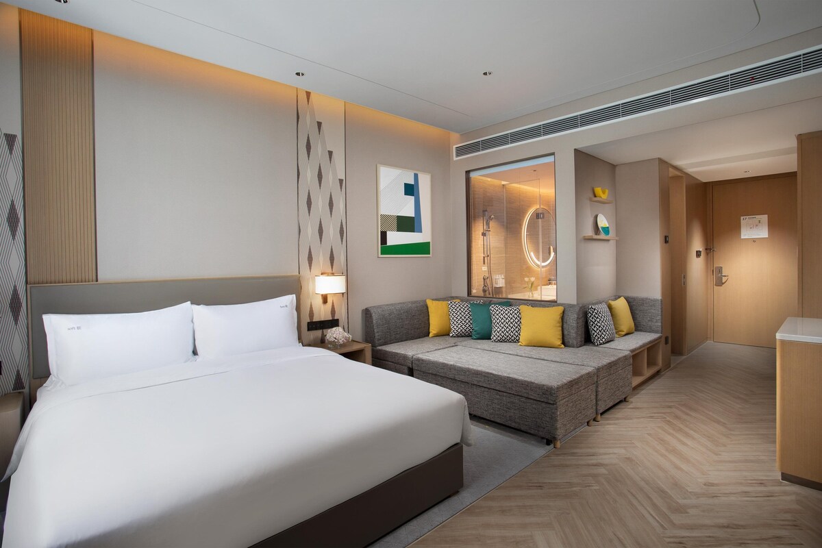 Una habitación de hotel con una cama grande, un sofá, un espejo y una pequeña kitchenette.