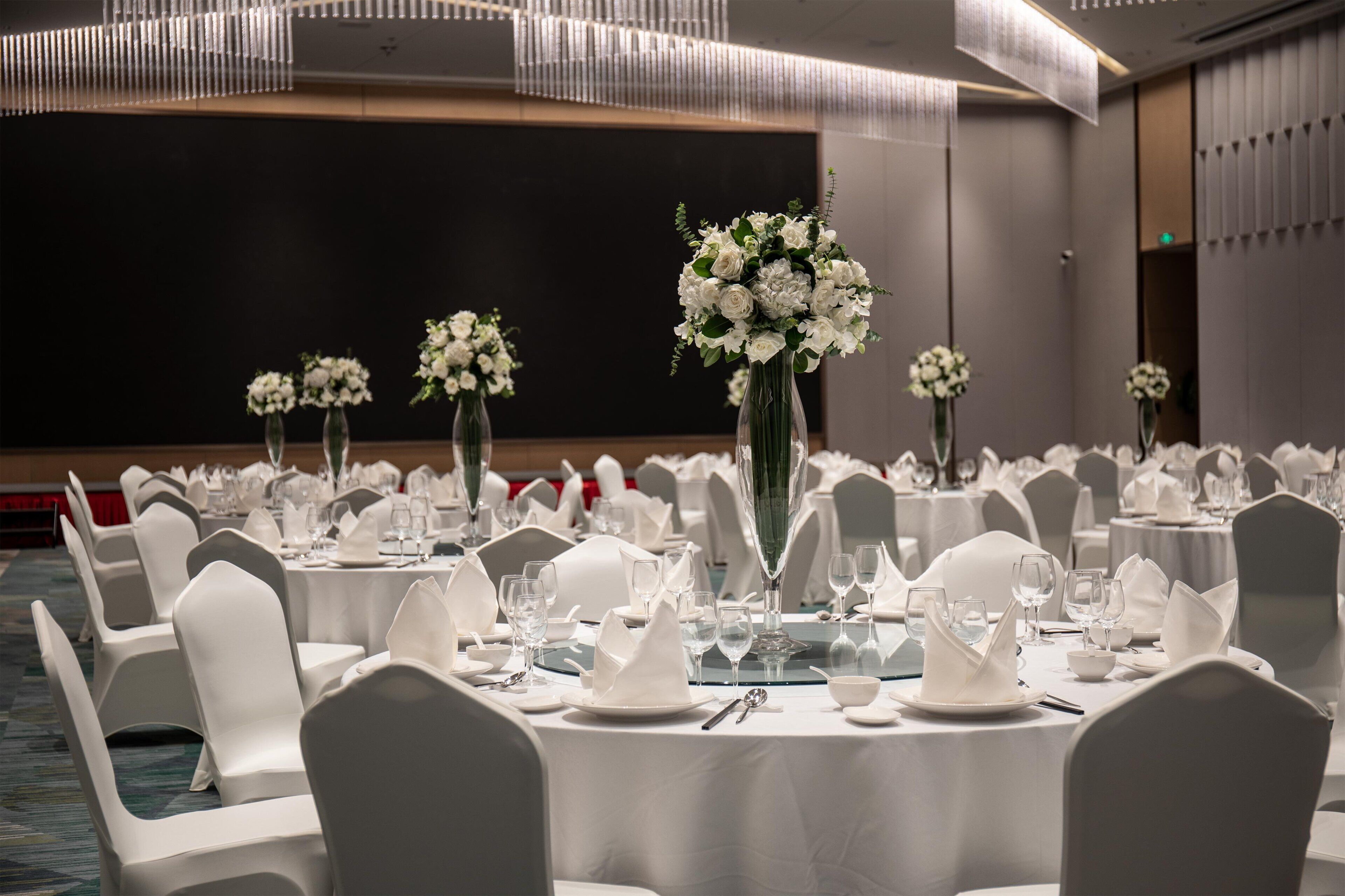 A banquet hall with round tables set for dining, white chairs, and floral centerpieces.