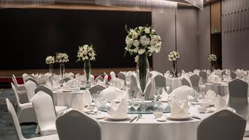 A banquet hall with round tables set for dining, white chairs, and floral centerpieces.