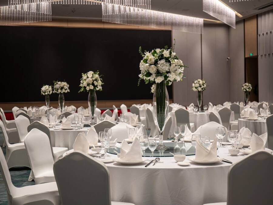 A banquet hall with round tables set for dining, white chairs, and floral centerpieces.