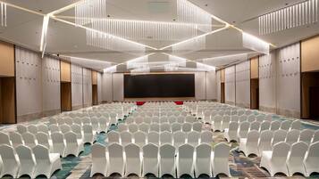 A conference room with rows of white chairs, a large screen, and modern lighting fixtures.