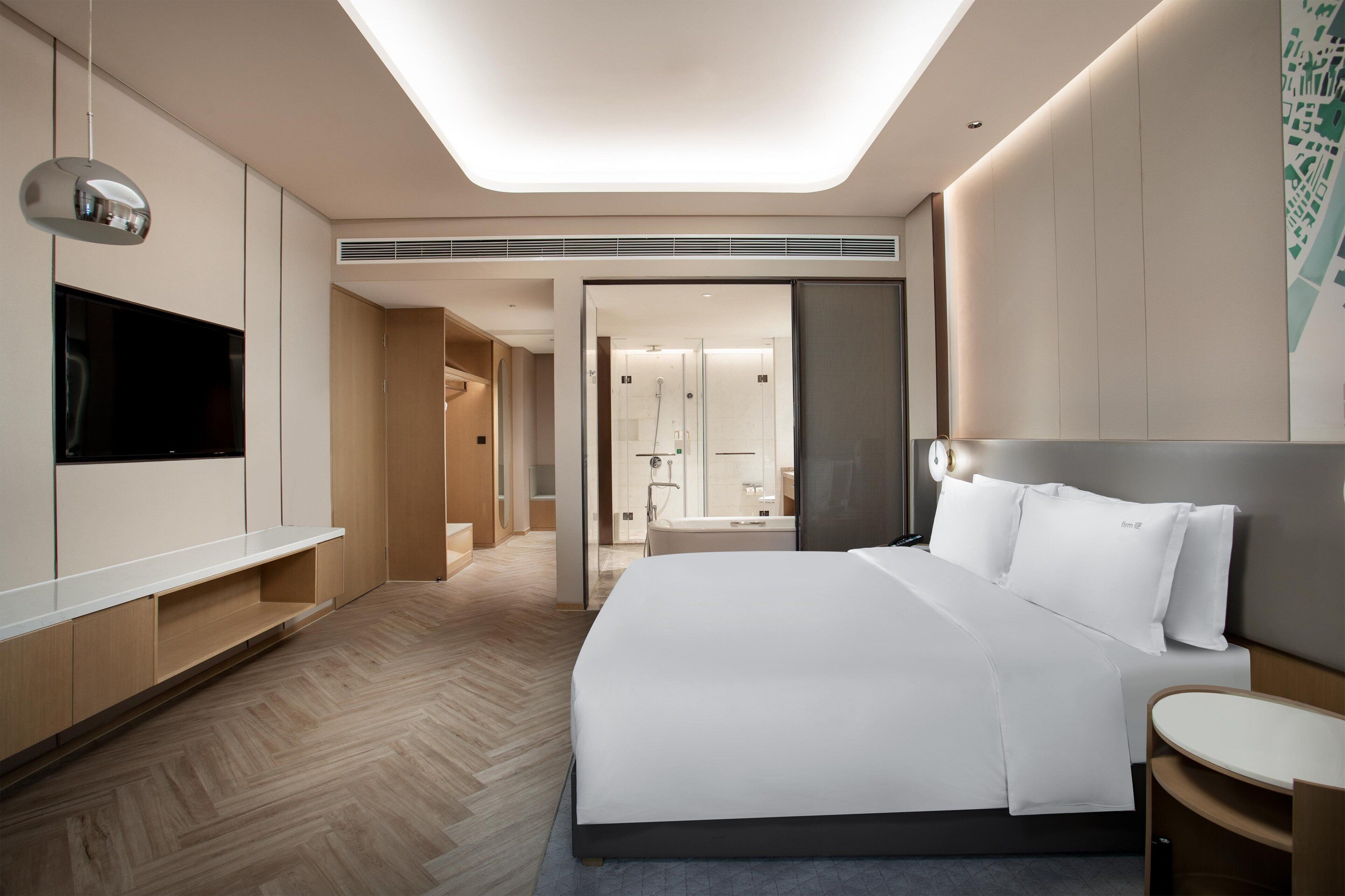 Ein modernes Hotelzimmer mit einem großen Bett, einem Flachbildfernseher, einem Schreibtisch und einem begehbaren Kleiderschrank.