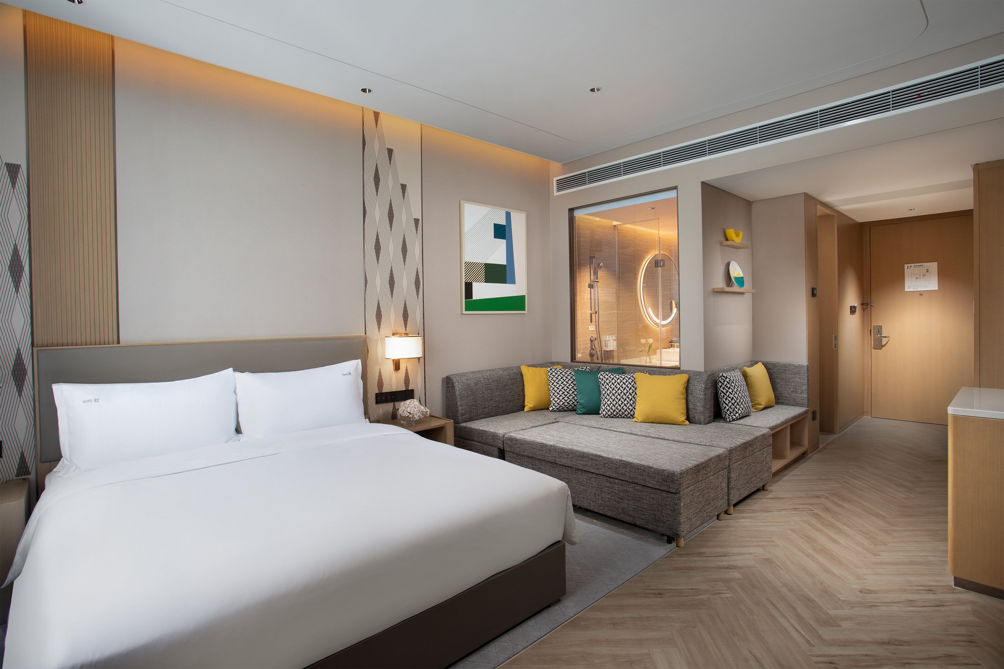 A hotel room with a large bed, a sofa, a mirror, and a small table with a lamp.