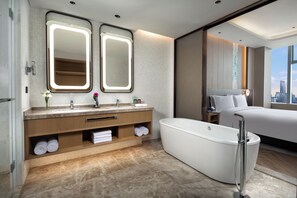 Un baño de hotel moderno con una bañera independiente grande, un tocador con espejos dobles y vistas a la ciudad.