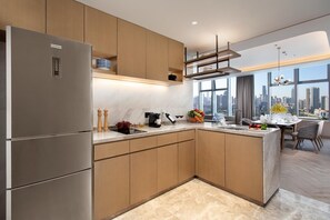 Una cocina moderna con refrigerador empotrado, armarios de madera, encimera de mármol y vistas a la ciudad a través de amplias ventanas.