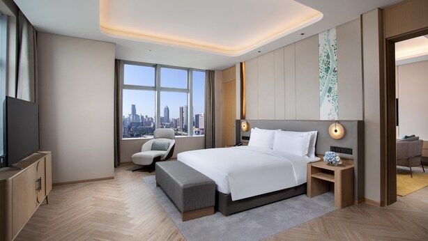 Una moderna camera d'albergo con un ampio letto, una televisione, una scrivania e vista sullo skyline della città.