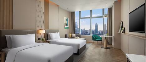 Habitación de hotel con dos camas, televisión, escritorio y vistas al horizonte de la ciudad.