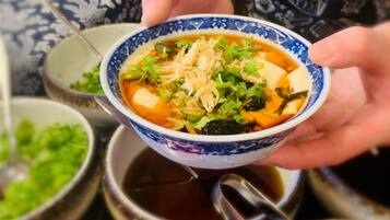 A bowl of soup with various ingredients, held by a person.