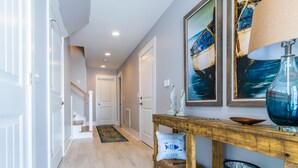 A hallway with a wooden console table, a welcome pillow, and two framed seascapes. - Brand NEW! | Luxury Townhome | 2 Master Suites | Elevator | Pool and ocean view (Kure Beach)