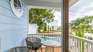 A balcony with wicker chairs and a small table, overlooking a pool and greenery. - Brand NEW! | Luxury Townhome | 2 Master Suites | Elevator | Pool and ocean view (Kure Beach)