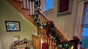 A staircase with a wooden railing, decorated with a garland and red ribbons. A red chair is placed near the bottom of the stairs. - Historical home, the Burnett Nestt in the heart of Lake Ann  (Lake Ann)