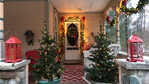 A porch decorated with Christmas trees, lanterns, and garlands. - Historical home, the Burnett Nestt in the heart of Lake Ann  (Lake Ann)