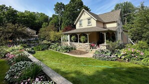 A two-story house with a stone foundation and a wrap-around porch. - Historical home, the Burnett Nestt in the heart of Lake Ann  (Lake Ann)
