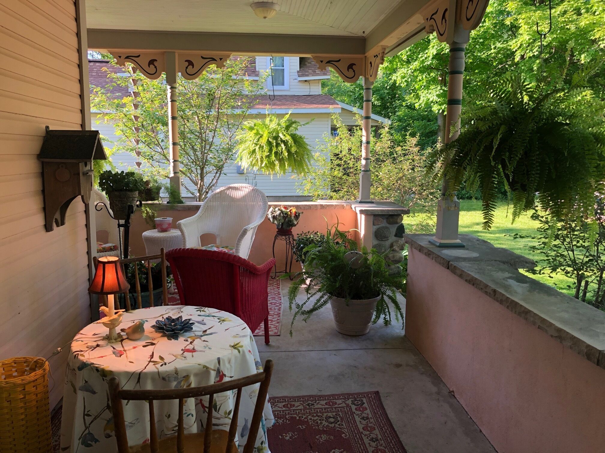 A covered patio with a table and chairs, surrounded by potted plants and a view of a house.