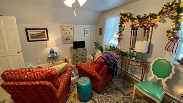 Una sala con sofás estampados, un pouf color turquesa y una silla verde. Se ve un televisor, una lámpara y un espejo decorativo.